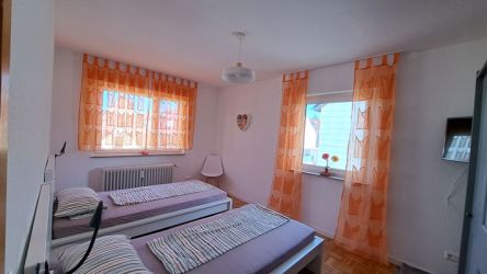 Helles Schlafzimmer mit zwei Einzelbetten, orangefarbenen Vorhängen und gemütlicher Atmosphäre.