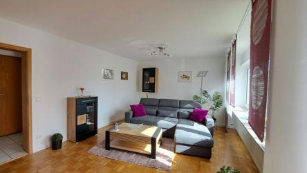 Modern eingerichtetes Wohnzimmer mit grauer Eckcouch, Couchtisch aus Holz und dekorativen Bildern an der Wand.